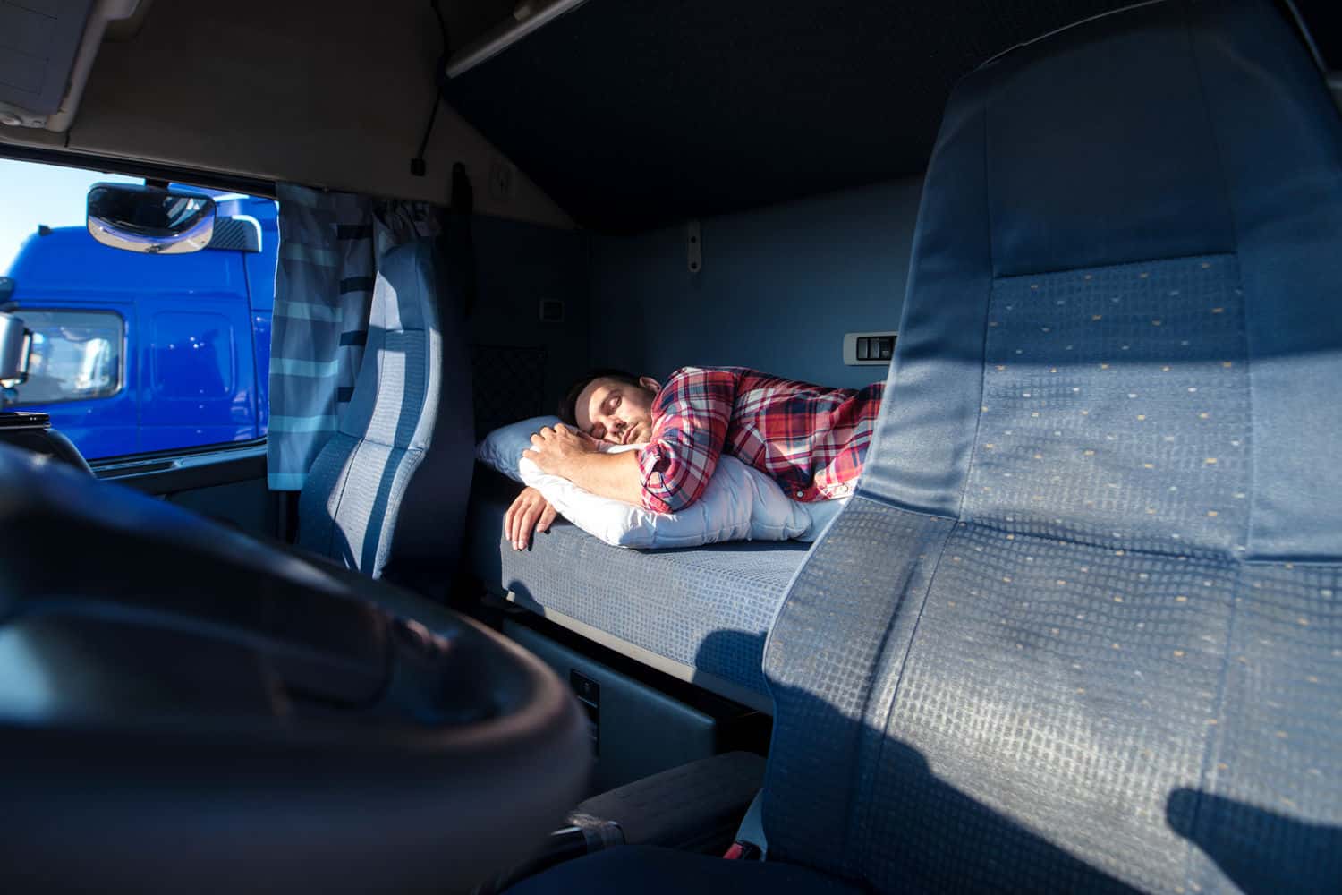 Man asleep on mattress behind the drivers seat in semi-truck